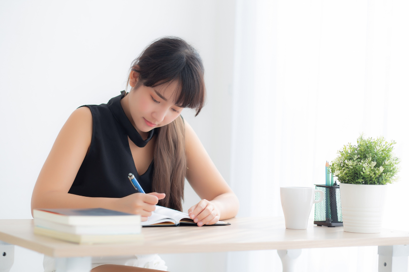 机に向かってノートに言葉を書き出す女性