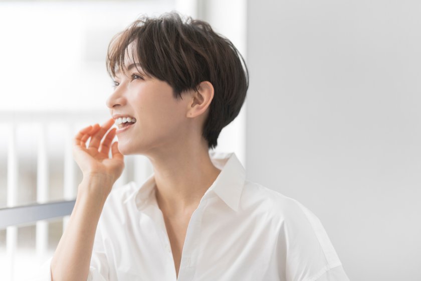 窓辺で笑顔を見せる白いシャツ姿の女性