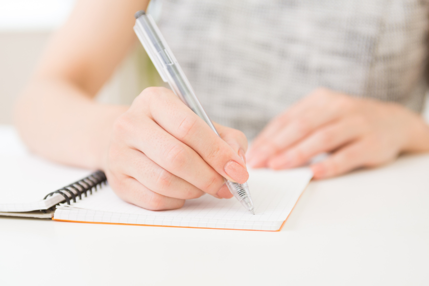 ノートにペンで書き込む手元。紙の使用を否定せずできる範囲で環境負荷を減らす考え方を表す画像