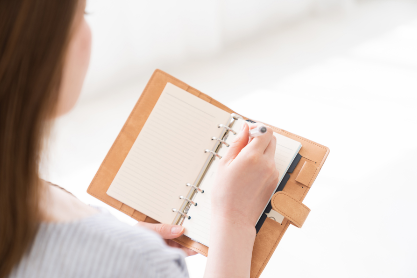 手帳にペンで書き込みをする女性の手元