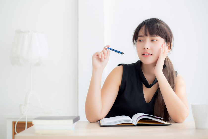 明るい室内でノートを前にペンを持ち、考えながら文章と向き合う女性