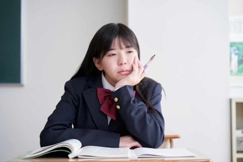 教室でノートを前に考え込む制服姿の女子生徒