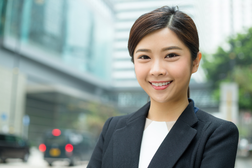 ビル街を背景に笑顔で立つスーツ姿の女性